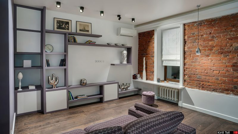 Работа Кирилла Толль — это исследование уюта как сложного, почти музыкального произведения. Его кадр выстроен на контрапункте текстур, где каждый материал ведет свою партию. Грубая, шершавая фактура состаренного кирпича звучит басом. Ему отвечает высокий, звонкий голос металлических плафонов светильников. Теплый, бархатный альт темного паркета поддерживается сухим, ритмичным шепотом геометрического узора на диване. Фотограф съемки интерьеров действует как дирижер, балансируя эти голоса через цвет: приглушенный серо-лиловый каркас мебели служит нейтральным медиумом, белый — паузой, точкой тишины. Даже свет здесь тактилен: точечные лучи выхватывают шероховатости кирпича, скользят по глянцу рам картин. Толль, московский фотограф с тонким чутьем к материи, показывает, что современный уют рождается не из единообразия, а из мастерского соединения диссонансов. Этот образ — наглядный аргумент для заказчика: интерьерная съемка высокого уровня способна зафиксировать не обстановку, а акустику пространства, его уникальный тембр.
