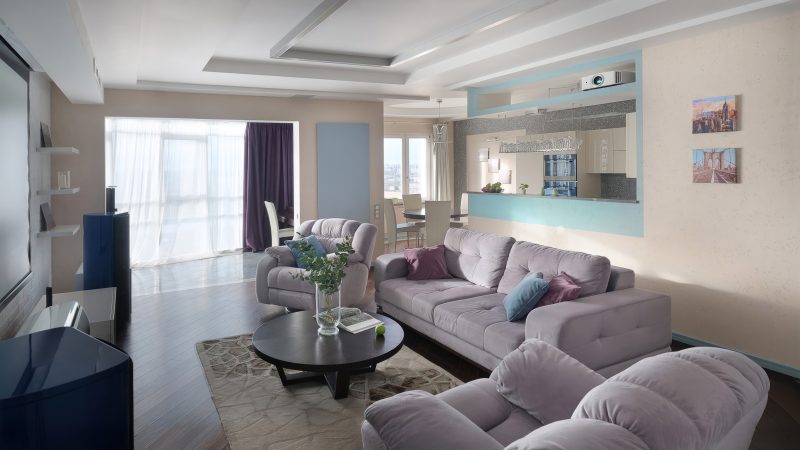 Интерьерная съемка гостиных в стиле современный минимализм рядом с метро Тушинская от фотографа Кирилл Толль. Пространство построено на гармонии объемов и чистых линий. Светлый диван с цветными подушками образует композиционный центр, вокруг которого выстраивается вся геометрия помещения. Большая прозрачная дверь создает эффект размытия границ, наполняя интерьер воздухом. Многоуровневый потолок со скрытой подсветкой парит над темным деревянным полом, создавая сложную световую партитуру. Фотограф мастерски использует цветовые акценты — синие и розовые подушки, голубая барная стойка, фиолетовая занавеска оживляют монохромную палитру. Кадр передает атмосферу современного урбанистического жилья.