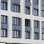 Фрагмент фасада: строгая геометрия окон и цветные решетки кондиционеров (серые, голубые, желтые).