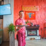 Официант в красном поло с подносом рядом с белым кирпичным порталом камина