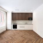 Съемка интерьера кухни-гостиной. Вид на кухонный гарнитур и обеденную зону. Контраст темного паркета и белой мебели.