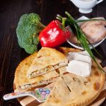 Осетинский пирог с начинкой из курицы и сыра на деревянной доске.