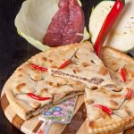 Осетинский пирог с мясной начинкой, украшенный красным перцем.