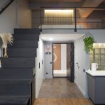 Входная зона лофта в ЖК Loftec: чёрная лестница на антресольный этаж, кухня со стеклоблоками и встроенные белые шкафы — фото Кирилла Толль