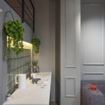 Кухня в ЖК Loftec: белая столешница на фоне стены из стеклоблоков с внутренней подсветкой и переход в гостиную с серым диваном — Кирилл Толль