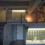 Панорамный вид двухуровневого лофта в ЖК Loftec: чёрная металлическая лестница, спальня на втором ярусе, кухня с подсвеченными стеклоблоками и бетонные балки на потолке — съёмка Кирилла Толль