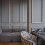 Уютная зона отдыха в ЖК Loftec: серые стены с классическими молдингами, низкий серый диван и белое плетёное кресло у рабочего стола — Кирилл Толль