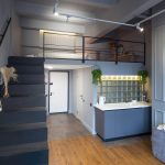 Двухуровневый лофт в ЖК Loftec со спальней на антресоли, чёрной металлической лестницей, серой кухней со стеклоблоками и трековым потолочным освещением — съёмка Кирилла Толль