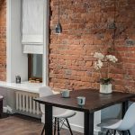 Обеденная зона в квартире у метро Трубная — тёмный стол, белые стулья Eames, хромированные подвесы и стена из красного кирпича. Фото: Кирилл Толль