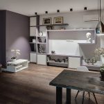 Общий план гостиной и обеденной зоны у метро Трубная — кирпичная стена, сиреневая стена, встроенный стеллаж и обеденный стол. Фото: Кирилл Толль