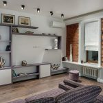 Общий вид гостиной с кирпичной стеной, встроенным стеллажом и диваном у метро Трубная — фото Кирилла Толль