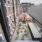 Панорамный вид из окна ЖК Loftec на внутренний двор с деревьями в кадках, кирпичными фасадами и пожарными лестницами — фото Кирилла Толль