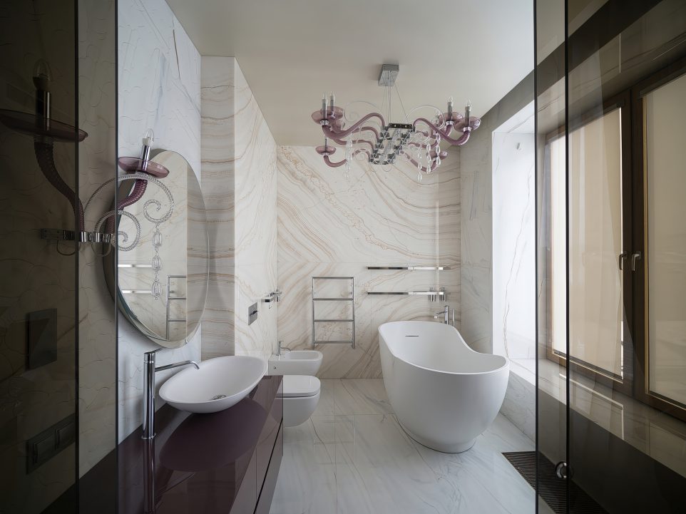 Светлая ванная комната с отделкой розовым мрамором, отдельно стоящей ванной-чашей, люстрой из розового стекла и большим окном.