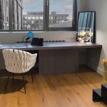 Современная рабочая зона у панорамного окна в ЖК Loftec с длинным серым столом, белым плетёным креслом, планшетом, микрофоном и зеркалом в углу — фото Кирилла Толль