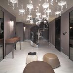 Интерьер роскошного холла с винтовой лестницей, зеркальными стенами, дизайнерской люстрой-инсталляцией из хрусталя и декоративными пуфами в форме гальки.