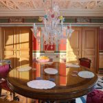 Симметричный интерьер столовой в ЖК Новопесковский на Арбате: круглый антикварный стол, муранская люстра, двойные деревянные двери и античные фрески в лучах закатного солнца — Кирилл Толль