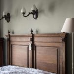 Изголовье кровати из темного массива дерева с резными элементами, классические настенные бра и торшер.