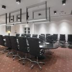 Широкоугольный рапомним зал заседаний Radisson Collection с вытянутым овальным столом темного дуба, хромированными крестовинами кресел на колесах и четырьмя параллельными подвесными светильниками-рамами