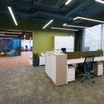 Панорамный вид на офис open space с оливковыми стенами, белыми столами и проходом в лаунж-зону, интерьерная фотосъемка Кирилла Толль