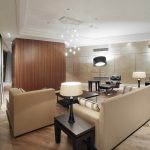 Просторная гостиная с деревянными панелями, креслом Eames и каскадной люстрой.