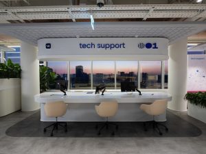 Фронтальный вид на стойку IT-поддержки и рабочие места в современном офисе VK Tech Support с большими панорамными окнами в начале заката.