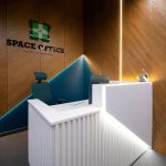 Зона рецепции Space Office с объемным подсвеченным логотипом зеленый крест на стеновых деревянных панелях шпона дуба угловой бирюзовой нишей со светодиодной лентой
