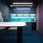 Фронтально боковой ракурс зоны ресепшн The Cube со светящимися гранями белой фрезерованной стойки бирюзовым креслом монитором компьютера серым ковровым покрытием