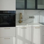 Детальный вид кухни в ЖК Level Причальный: матовые белые фасады с латунными ручками, золотой смеситель, фартук под мрамор.