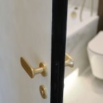Деталь интерьера в ЖК Level Причальный: матовая золотая дверная ручка на белой двери с черным торцом.
