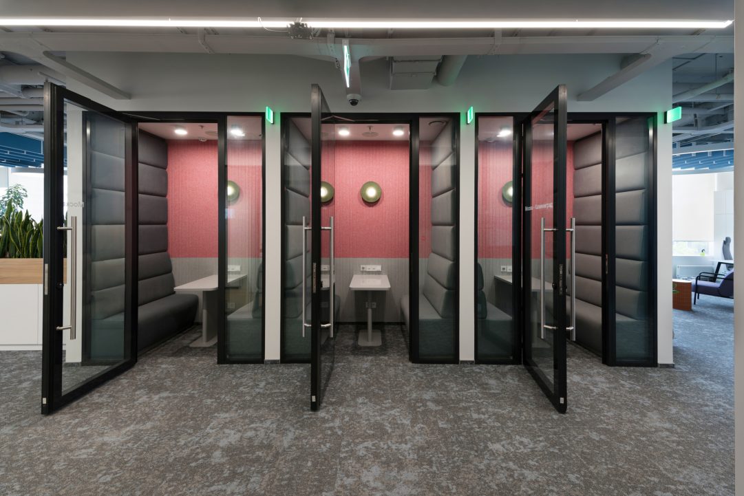 Индивидуальные переговорные кабины Meeting Pods в офисе VK со звукоизоляционными акустическими панелями, стеклянными фасадами и темным ковролином.