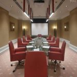 Фронтальный вертикальный кадр переговорной Radisson Украина с красным кожаным креслом по центру переднего плана, глянцевым столом зебрано, потолочным белым проектором и картинами в золотистых рамах
