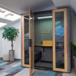 Высокий переговорный стол со светлыми барными креслами и подвесной акустической перегородкой на фоне кирпичной стены в БЦ Лотос, фотограф Кирилл Толль
