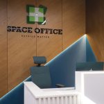Крупный план деревянной бренд стены со шпоном дуба подсвеченным логотипом Space Office глубокой скошенной бирюзовой нишей кристалл краем белой рифленой стойки