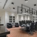 Панорама зала Radisson с длинной консолью темного дерева, настольной лампой с салатовым конусообразным абажуром, вешалкой-стойкой в углу, черным овальным столом и потолочными кубическими спотами