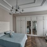 Интерьер светлой спальни в ЖК Грин Плаза. Встроенный шкаф с зеркалами в классическом стиле, кровать с высоким стеганым изголовьем и паркет французская елка.