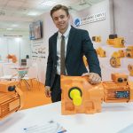 Профессиональный мужчина модель на выставочном стенде Starshine Drive позирует с промышленным мотор-редуктором, пример рекламного репортажа выставки