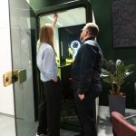 Крупный план снизу вверх изнутри кабины. Демонстрация инженерного узла потолочной панели: белая перфорированная решетка принудительной приточной вентиляции, встроенные точечные LED-светильники и датчик движения. В углу виден стык звукоизоляционных панелей, обтянутых серым фетром.