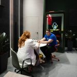 Жанровый двухфигурный кадр. Менеджер с рыжими волосами сидит за круглым столом переговоров напротив представителя компании-партнера Троя. Гость держит ручку над блокнотом, внимательно слушая спецификации материалов. На столе установлены брендированные бутылки воды Space Office.