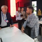 Крупный репортажный план. Рустем Мамин ведет диалог один на один со статусным гостем выставки, слегка облокотившись на спинку сетчатого офисного кресла. Контрастный задний фон павильона МТС Live Холла с яркой красной колонной эффектно обособляет фигуры спикеров переднего плана.