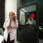 Горизонтальный кадр функционального дуэта. На переднем плане слева в резкости находится улыбающаяся сотрудница с ежедневником. Справа на среднем плане за прозрачным стеклом кабины зафиксирован Денис Силавин со смартфоном в руках, демонстрируя сценарий конфиденциального звонка.
