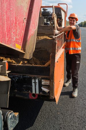 Рабочий контролирует укладку асфальта, внимательный взгляд