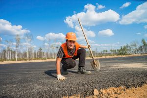 Фото сотрудника на рабочем месте. Пример производственной съемки для компании Рабочий проверяет уровень свежего асфальта, портрет в процессе