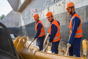 Трое строителей в касках синхронно работают, командная работа на объекте