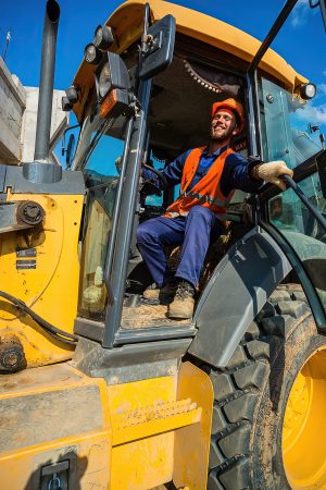 Машинист бульдозера, парень в каске позирует на фоне техники
