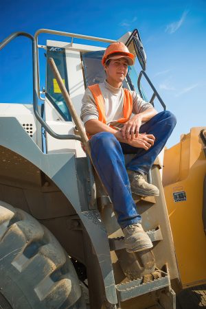 Молодой экскаваторщик в кабине техники, портрет на фоне заката