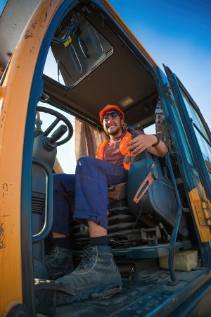 Оператор трактора, молодой рабочий в каске задумчиво смотрит в сторону